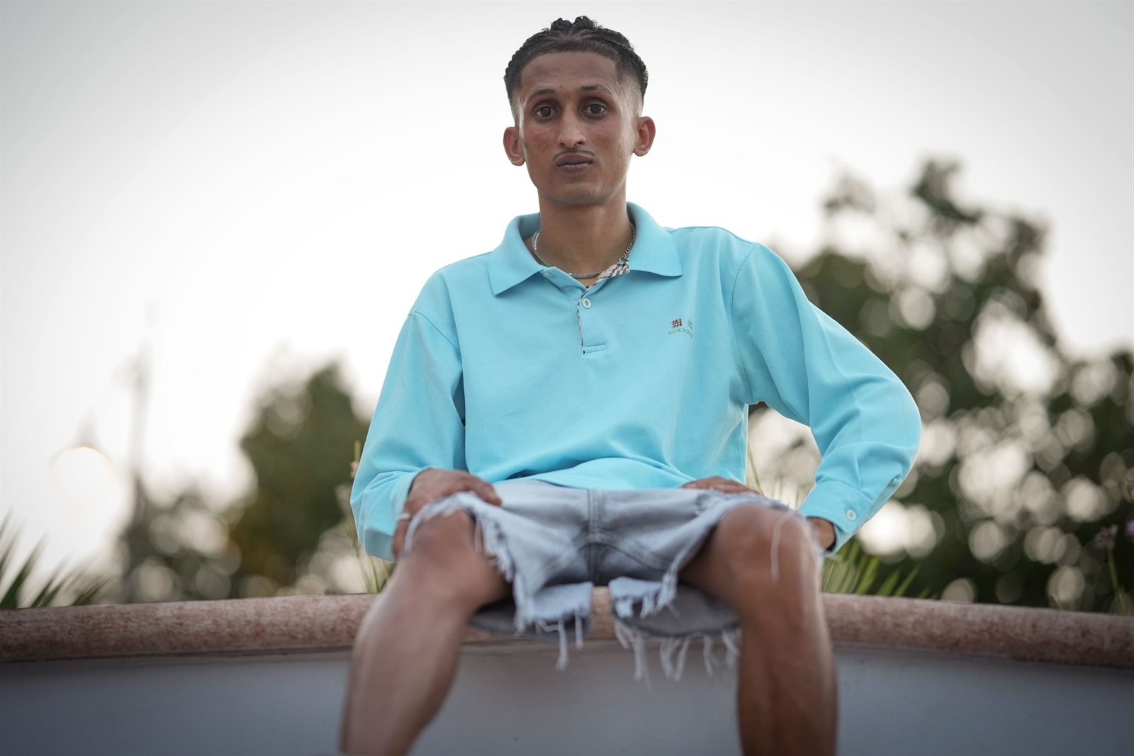 Fida Nadeem ripreso dal basso, seduto contro il cielo